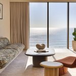 A modern, stylish living room with a view of the ocean, featuring a floral-patterned couch, a coffee table, and a potted