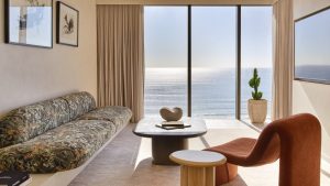 A modern, stylish living room with a view of the ocean, featuring a floral-patterned couch, a coffee table, and a potted